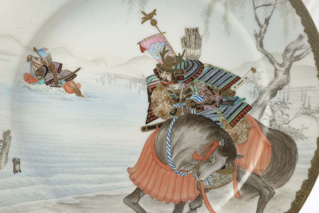 A close-up of an oval ceramic plate or dish featuring a hand-painted Japanese winter scene with a samurai on horseback and another figure in the snow.