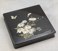 Close view of the white daisy and smaller flower decoration with a butterfly on the black lacquer lid