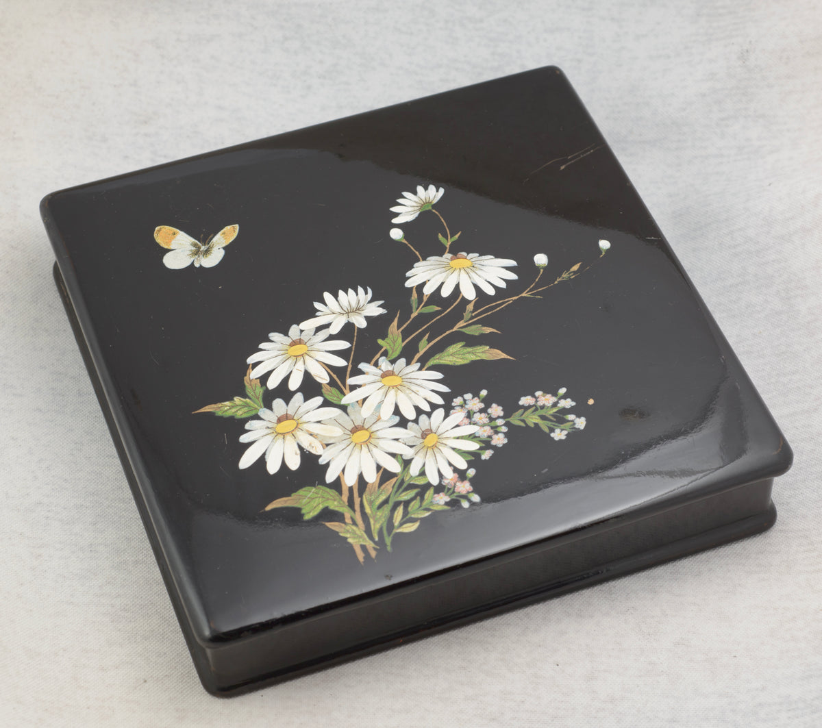 Close view of the white daisy and smaller flower decoration with a butterfly on the black lacquer lid
