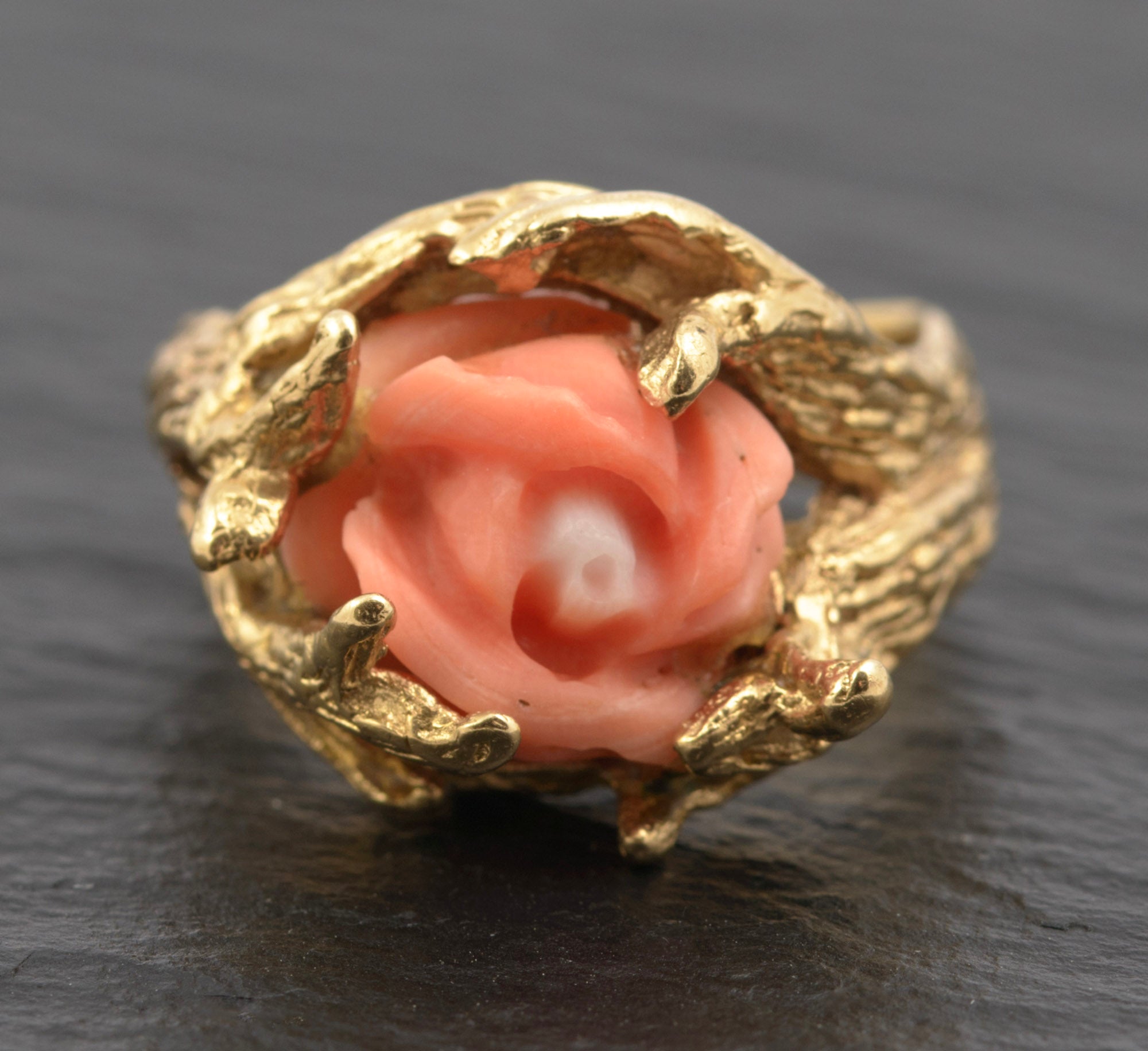 A vintage 14ct gold ring centred on a carved salmon coral rose, the flower held within a setting of textured gold fronds arranged as claws, mid-20th century.