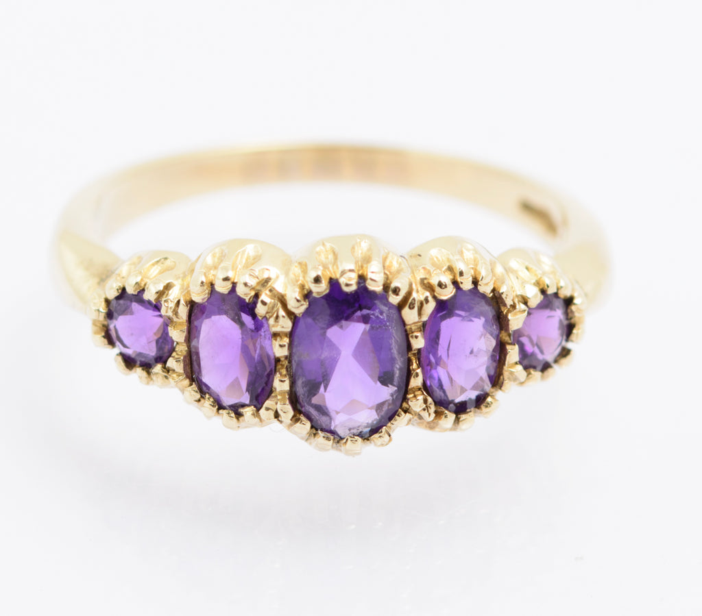 A vintage 9ct gold ring set with five graduated natural amethysts - three oval cut at the centre, two round cut at the shoulders - in a multi claw arrangement, hallmarked Birmingham, 1980s.