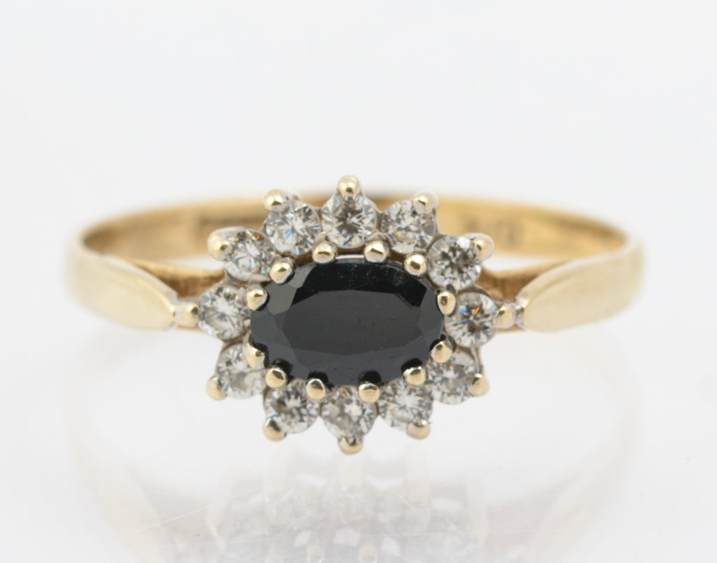 Gold ring with a central black gemstone and diamond-studded halo on a white background