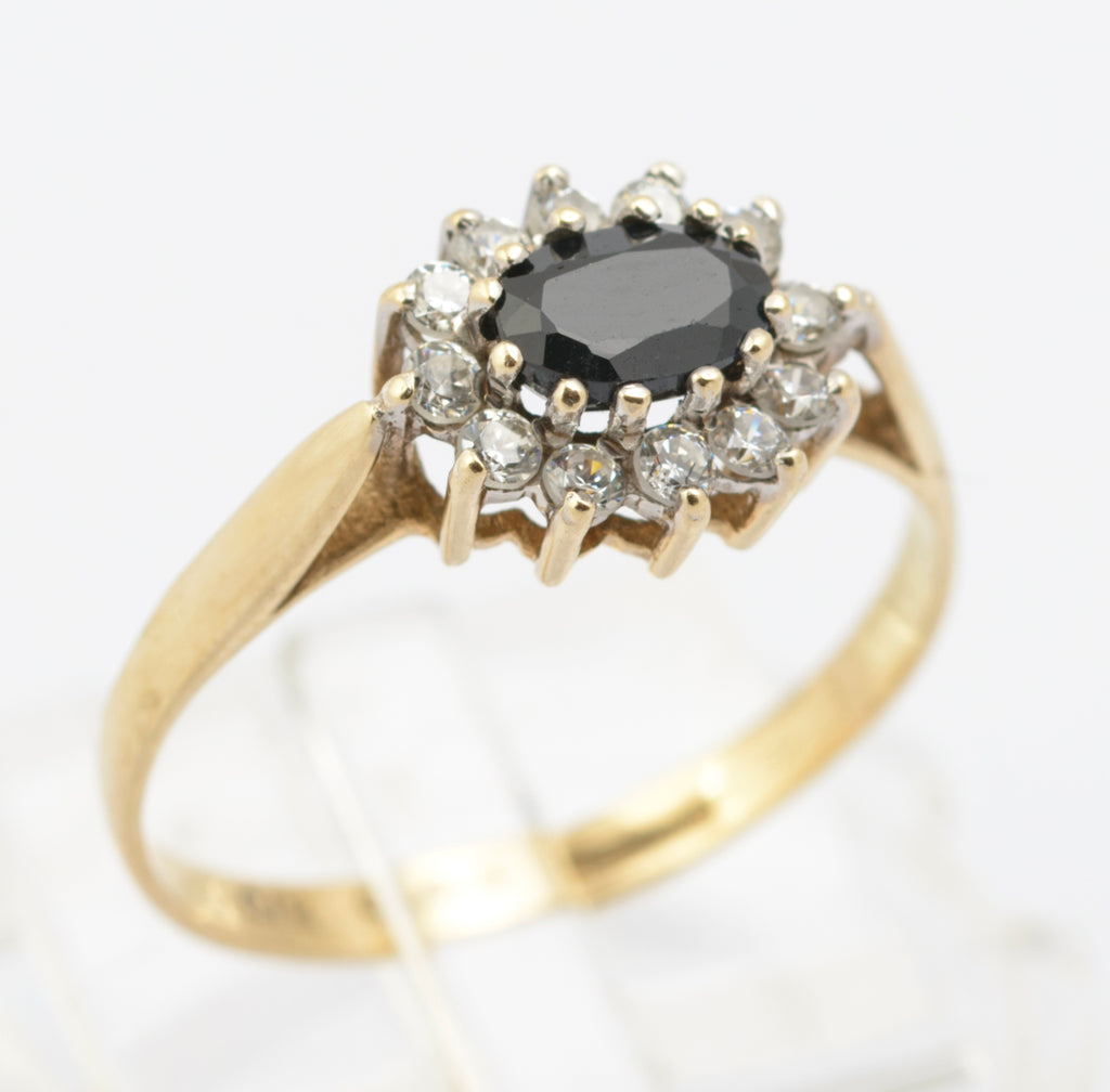 A vintage 9ct gold ring set with a natural midnight blue sapphire in an east-west orientation, surrounded by a CZ halo in a low cathedral mount with bifurcated shoulders, Birmingham hallmarked 1986.