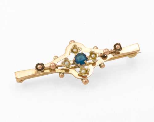 Antique 9ct gold bar brooch - front view showing open geometric frame with central blue glass stone in claw setting, four split seed pearls in flower settings and applied gold bead detail