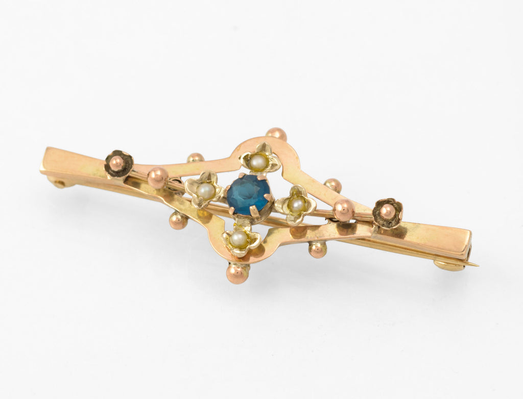 Antique 9ct gold bar brooch - angled front view showing layered open frame construction with blue glass centre stone and seed pearl flower settings