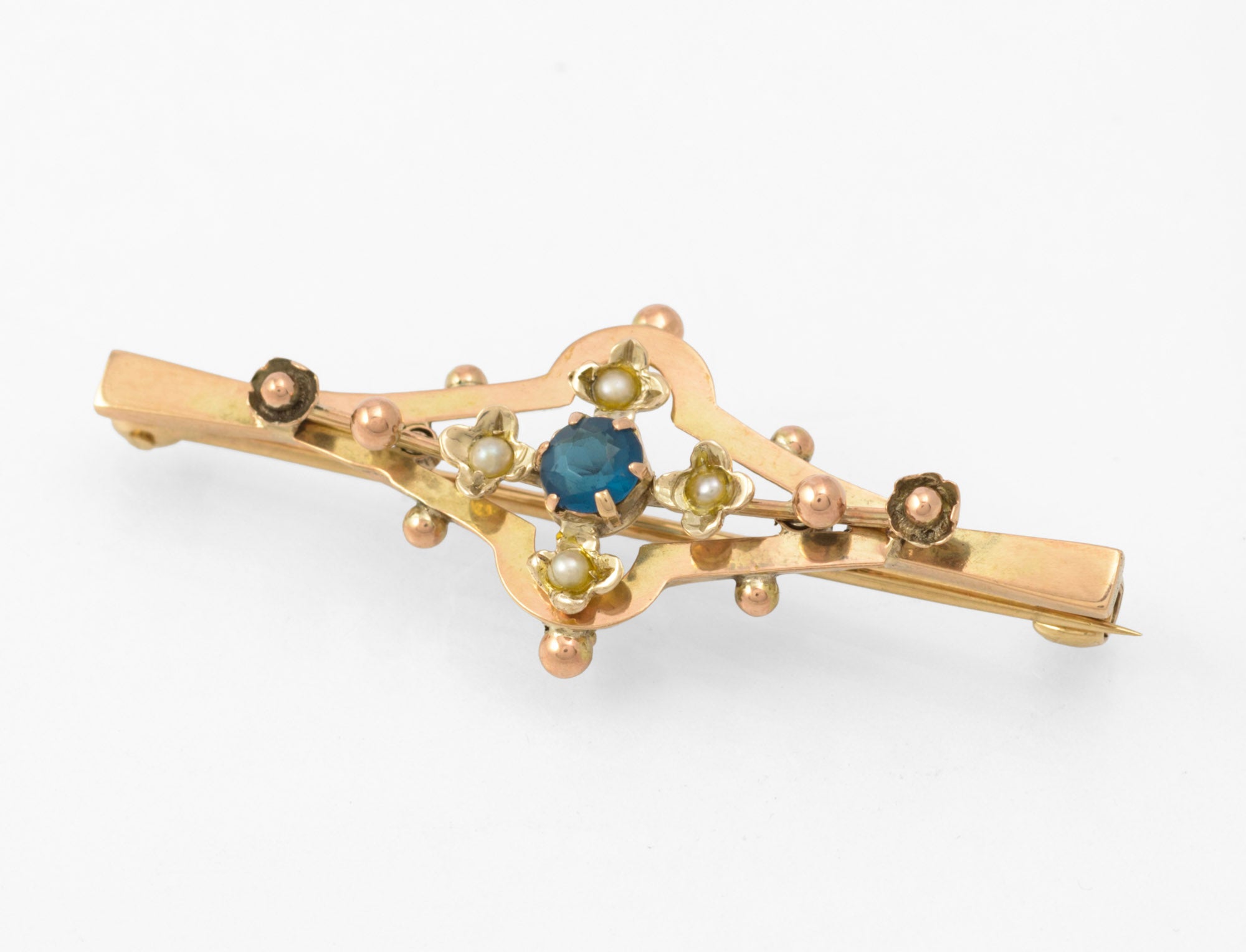 Antique 9ct gold bar brooch - angled front view showing layered open frame construction with blue glass centre stone and seed pearl flower settings