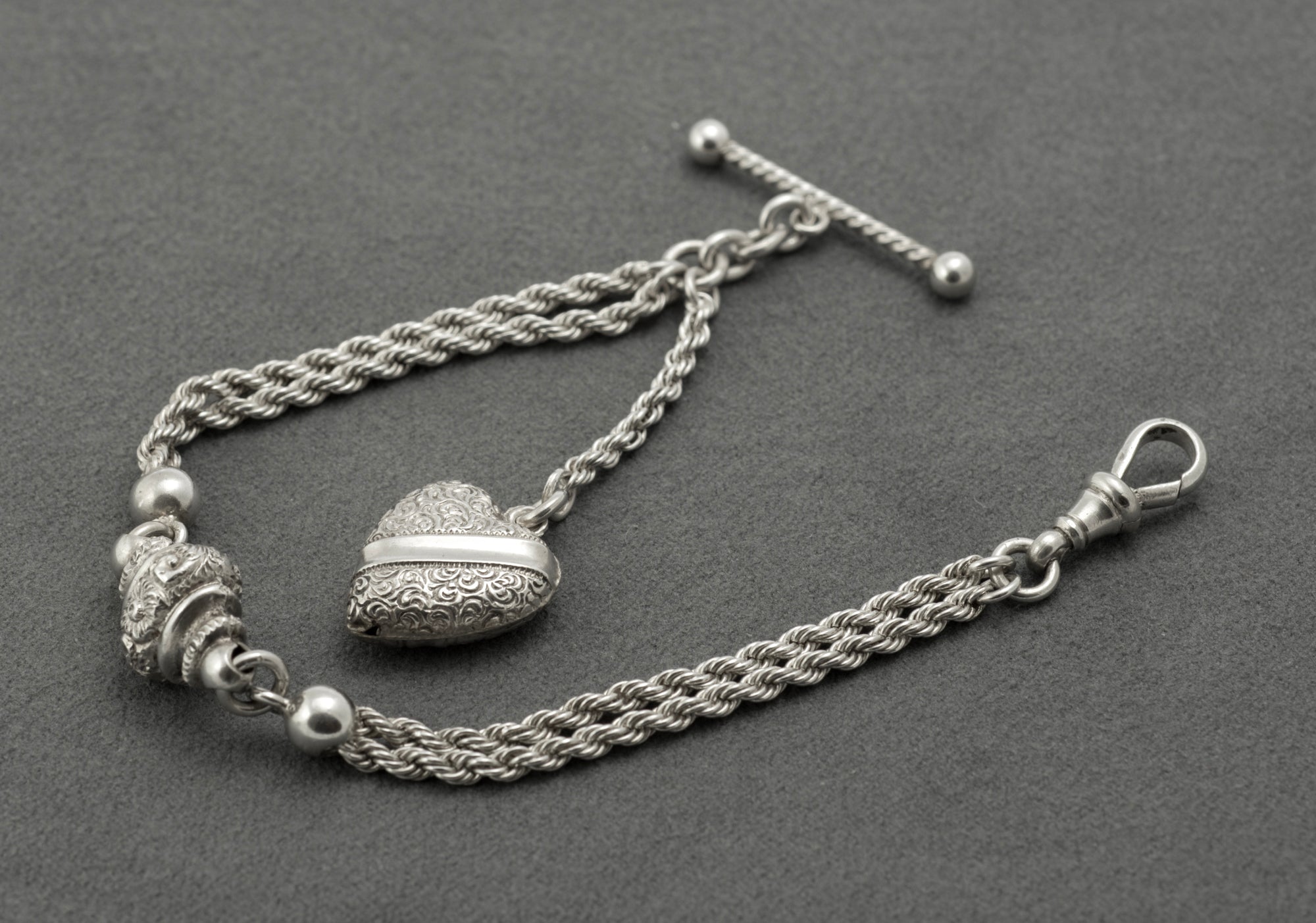 Antique Victorian sterling silver Albertina chain - close up of heart fob front showing dense scrolling decoration and plain central band on softly rounded form