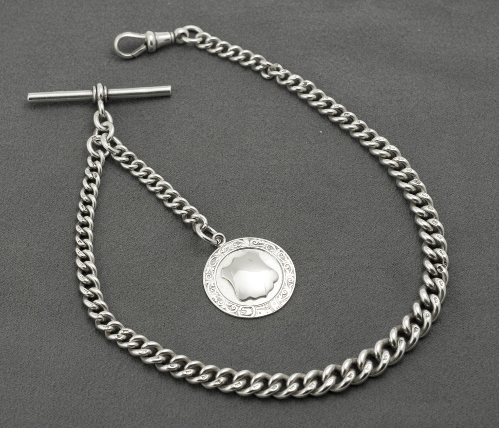 Antique Victorian sterling silver Albert chain - close up of fob face showing polished shield-shaped cartouche surrounded by engraved scrolling decoration