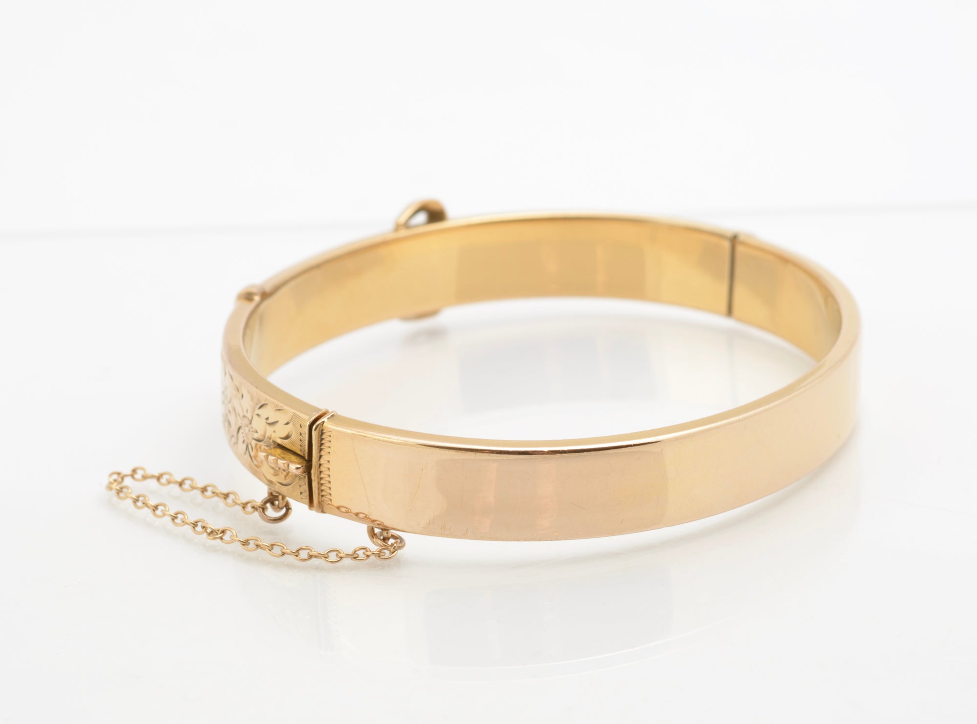Edwardian gold metal cored buckle bangle - three quarter front view showing buckle motif and engraved floral panels with safety chain