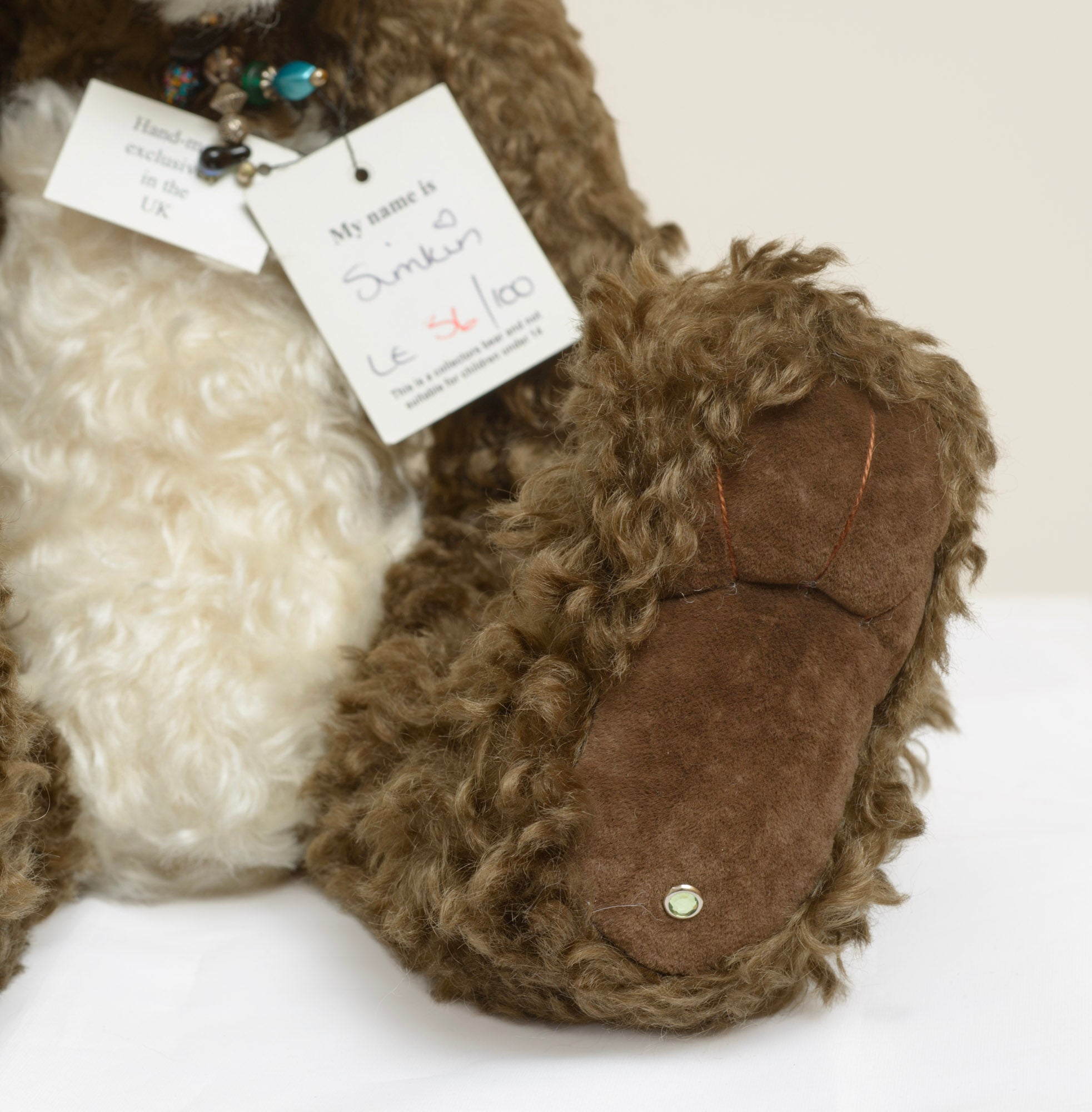 Kaycee Bears Simkin - Kelsey Cunningham - side view showing two-tone curly plush coat, cream face and tummy panel against dark chocolate body, with old gold bead necklace