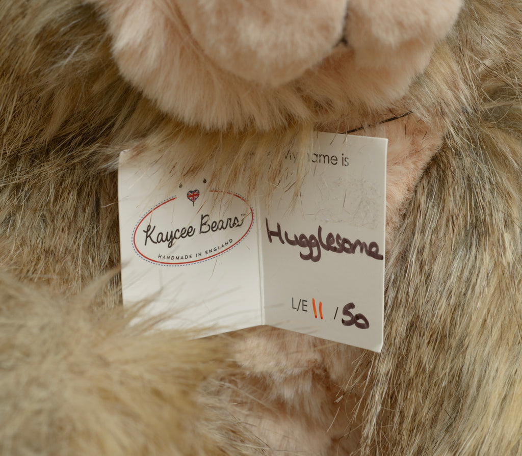 Kaycee Bears Hugglesome - Kelsey Cunningham - full front seated view showing two tone plush with long wild sandy taupe body and blush pink tummy panel, with name tag reading My name is Hugglesome 11/50