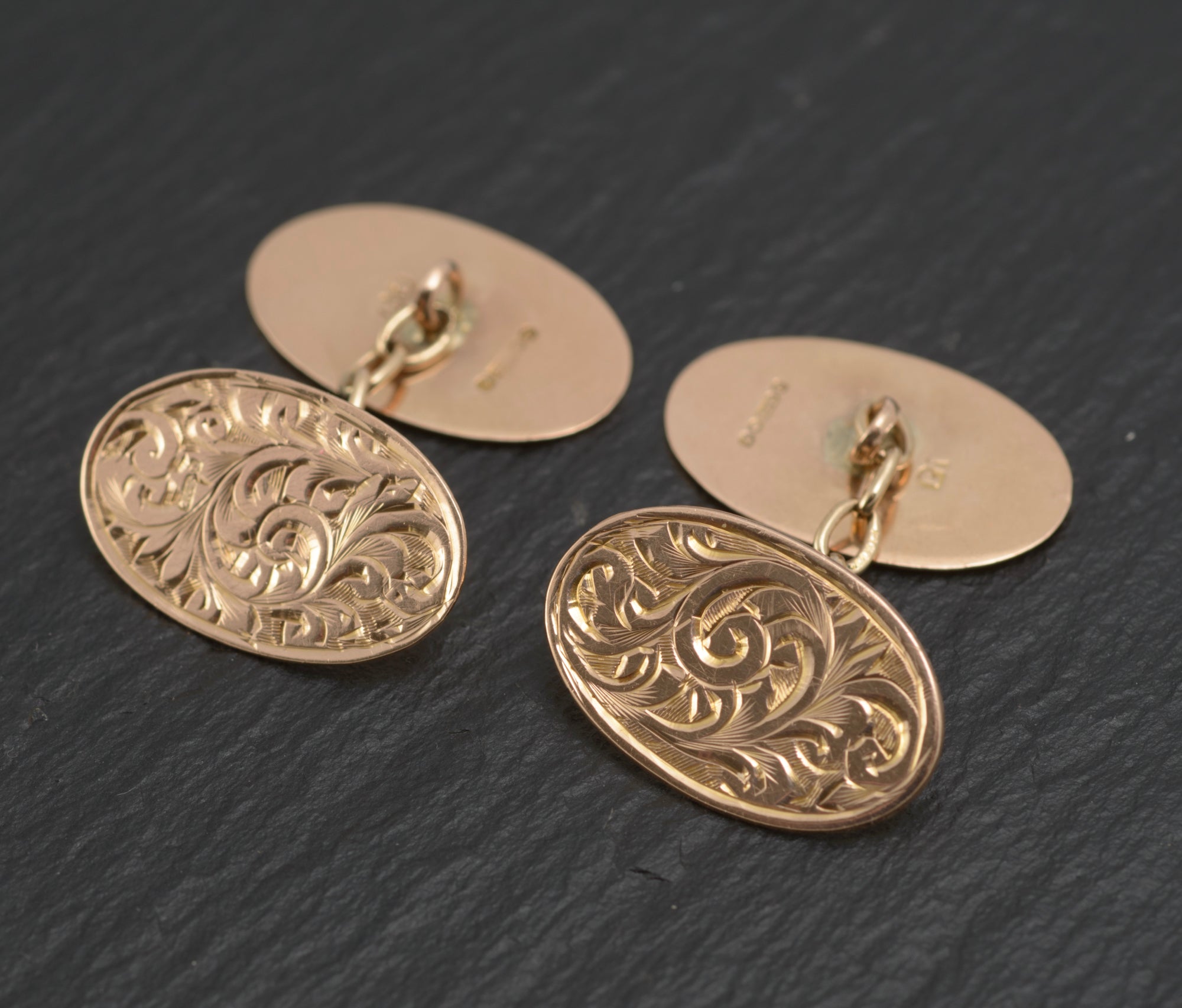 Antique 9ct light rose gold cufflinks - engraved foliate scrolls - three-quarter view showing both cufflinks with engraved front panels and plain reverse panels connected by chain links on dark slate background
