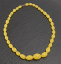 Art Deco uranium vaseline glass bead necklace - vivid opaque yellow - full view laid flat on dark slate showing graduating oval beads from small clasp end to large central oval bead