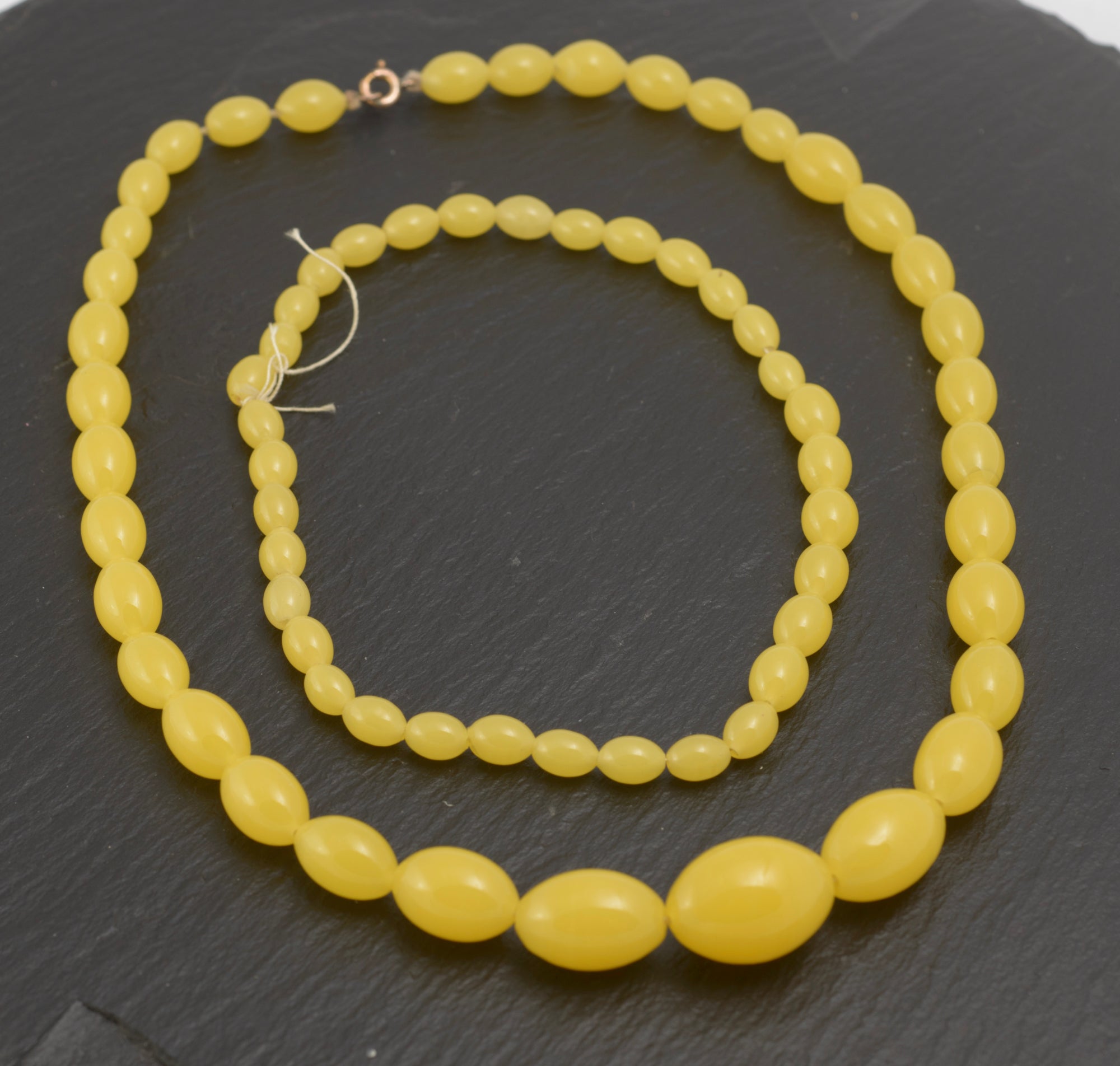 Art Deco uranium vaseline glass bead necklace - vivid opaque yellow - full view showing necklace alongside approximately 27cm of matching spare beads on dark slate background