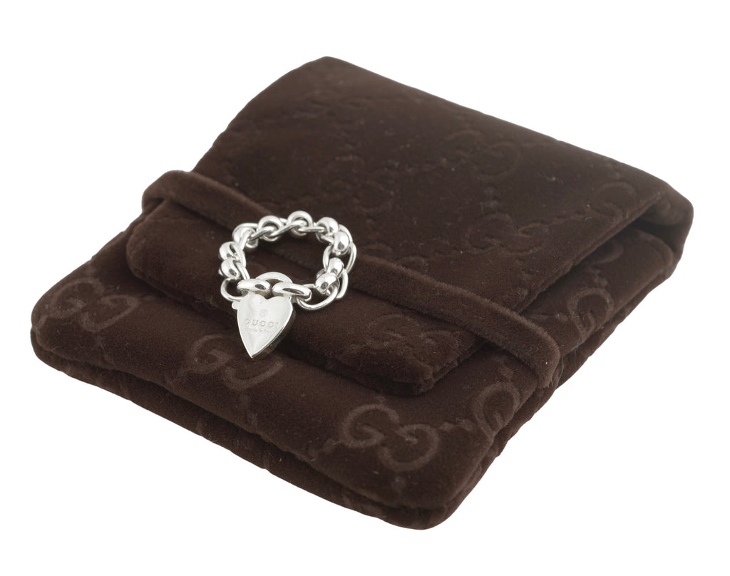 Gucci sterling silver chain link ring with heart charm - close up of ring on GG monogram soft brown pouch showing articulated oval rolo chain links and heart charm with Gucci engraving on dark background