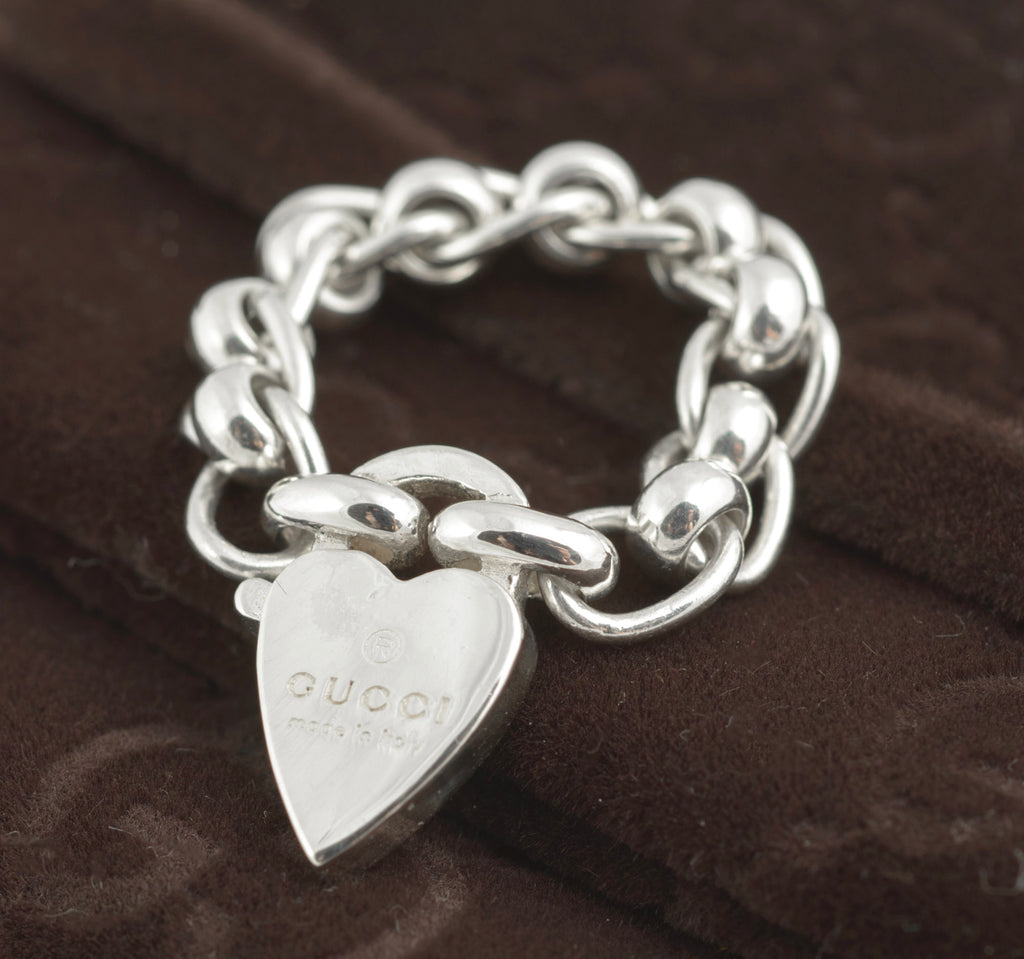 Gucci sterling silver chain link ring with heart charm - close up macro view showing polished oval rolo chain links and heart charm face engraved with Gucci name and made in italy text on dark background