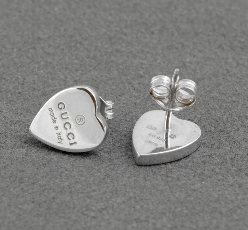 Gucci sterling silver heart stud earrings - made in Italy - one earring front showing Gucci engraving, one earring reverse showing AG 925 hallmark and Florence assay mark with post and butterfly back separated on grey background