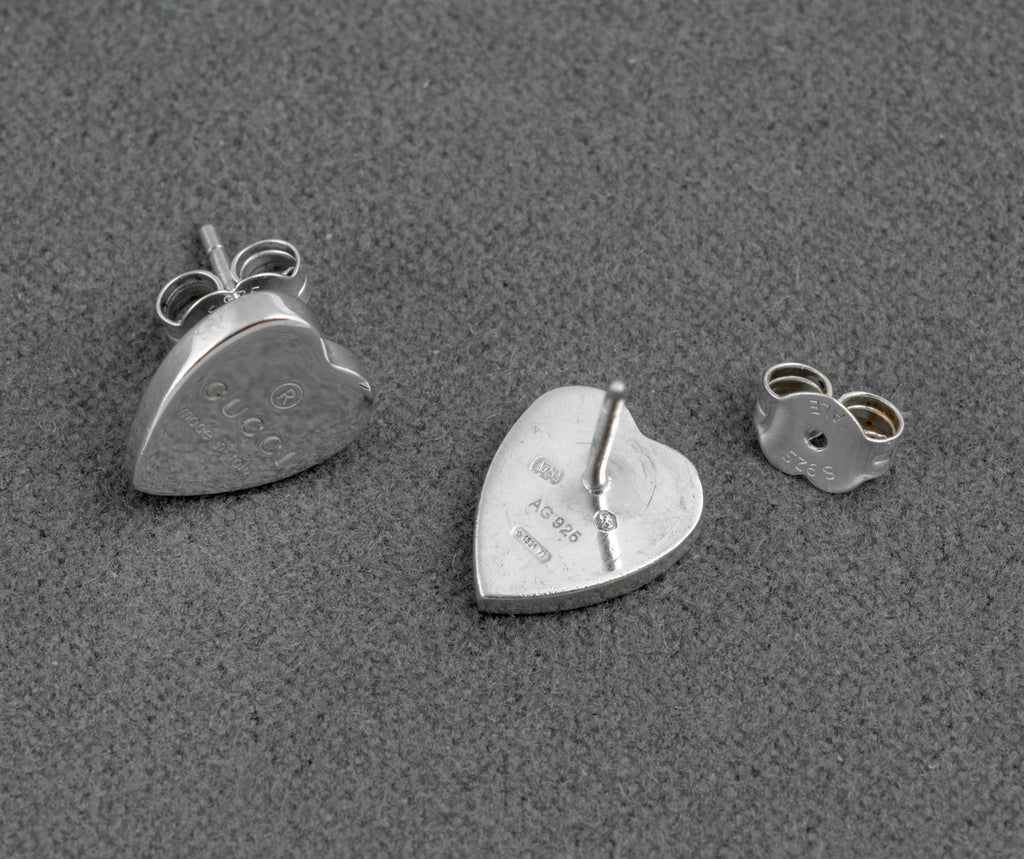 Gucci sterling silver heart stud earrings - made in Italy - three piece detail showing earring front with Gucci engraving, earring reverse with AG 925 mark, and butterfly back fitting separately on grey background