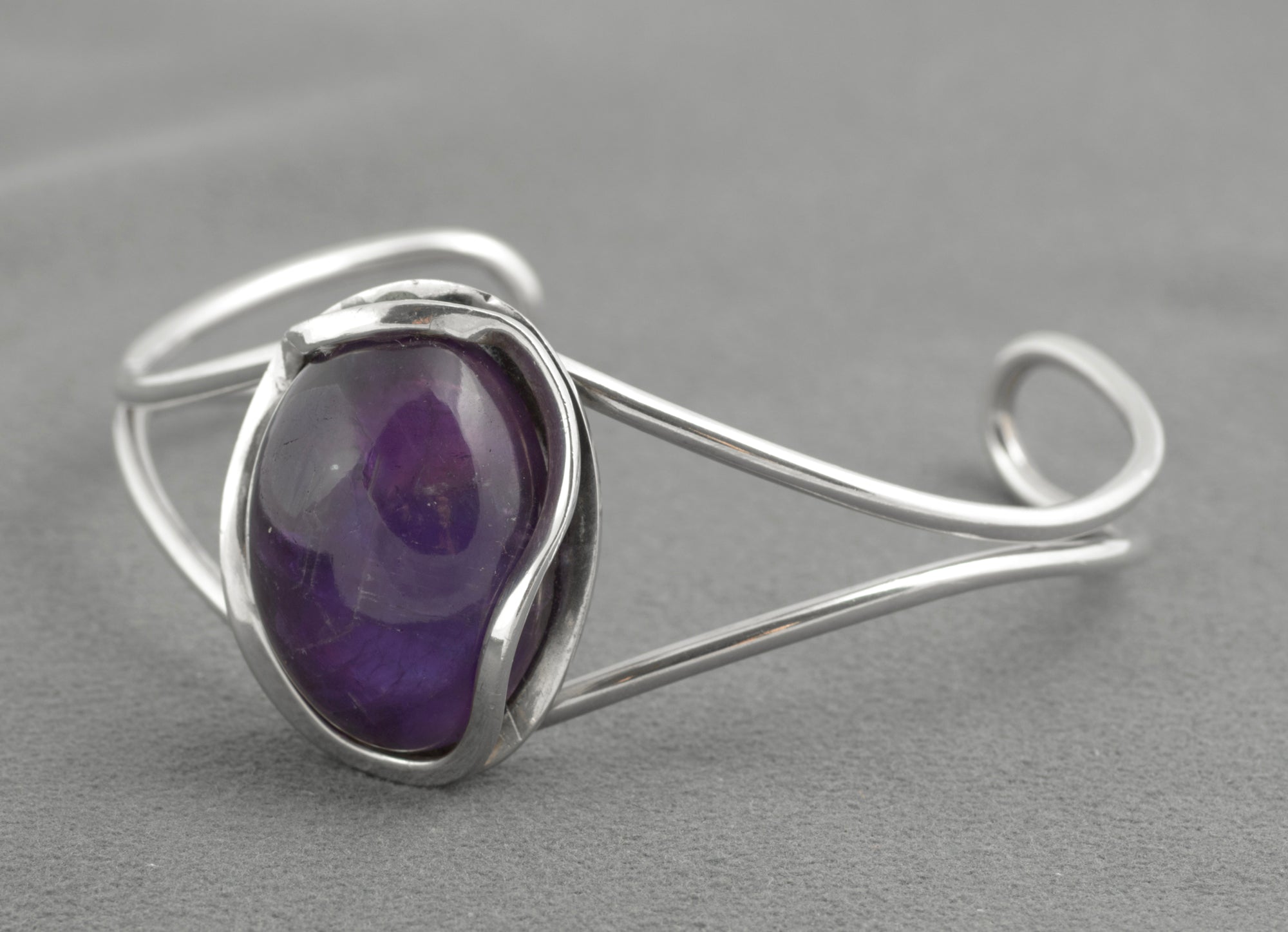 Vintage sterling silver amethyst cabochon bangle - Polish handmade - Gdańsk 925 - rear three-quarter view on grey background showing scrolled wire terminals and Gdańsk 925 hallmark struck to reverse of bezel with amethyst visible through open back setting