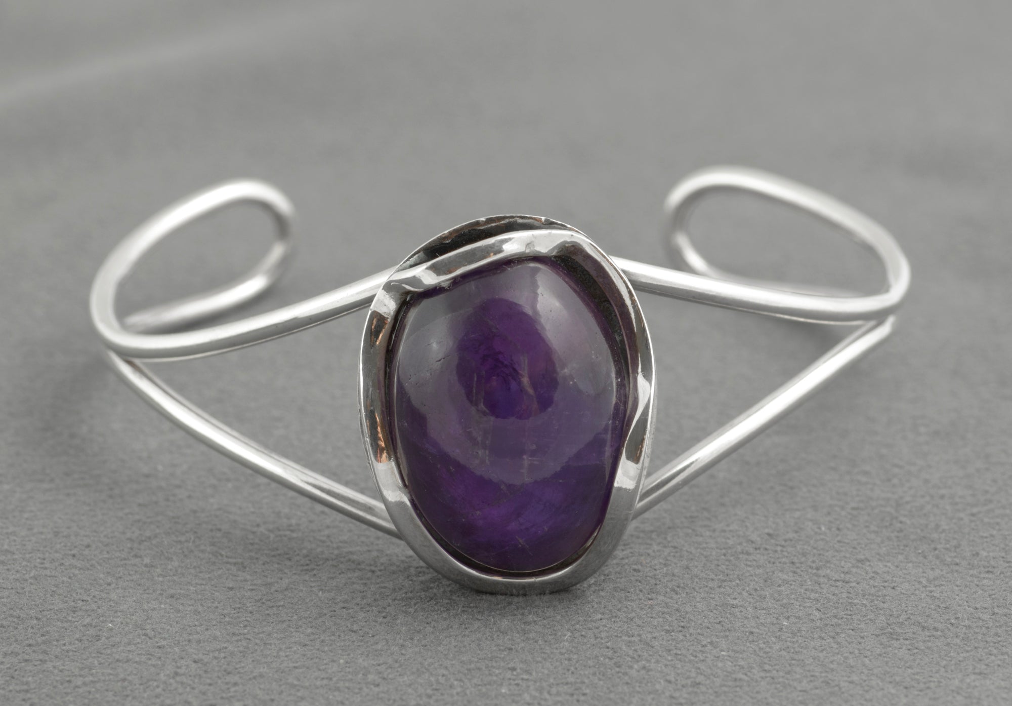Vintage sterling silver amethyst cabochon bangle - Polish handmade - Gdańsk 925 - three-quarter view on white background showing parallel wire arms curling to scrolled terminals and large amethyst cabochon in open bezel setting