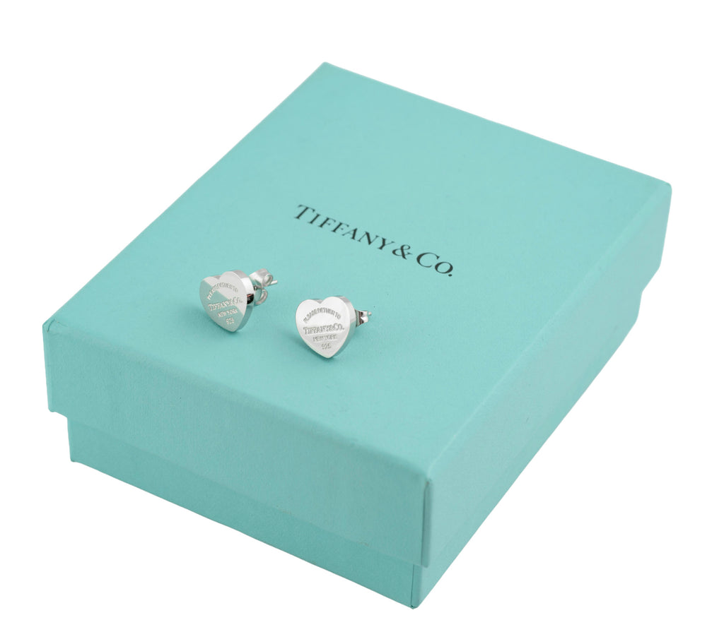 Pair of Tiffany and Co Return to Tiffany sterling silver heart stud earrings resting on closed Tiffany blue box showing engraved inscription to face of each earring