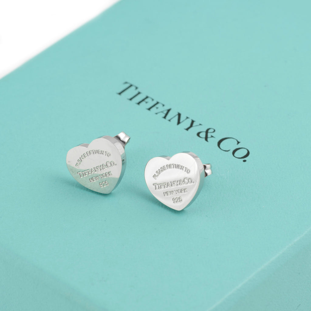 Close up of pair of Tiffany and Co Return to Tiffany sterling silver heart stud earrings on Tiffany blue box showing engraved Please Return To Tiffany and Co New York 925 inscription clearly on both earrings