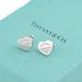 Close up of pair of Tiffany and Co Return to Tiffany sterling silver heart stud earrings on Tiffany blue box showing engraved Please Return To Tiffany and Co New York 925 inscription clearly on both earrings
