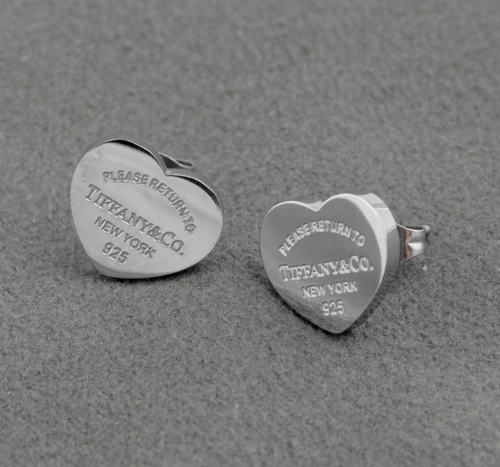 Pair of Tiffany and Co Return to Tiffany sterling silver heart stud earrings on grey background showing engraved inscription to face and butterfly back fittings