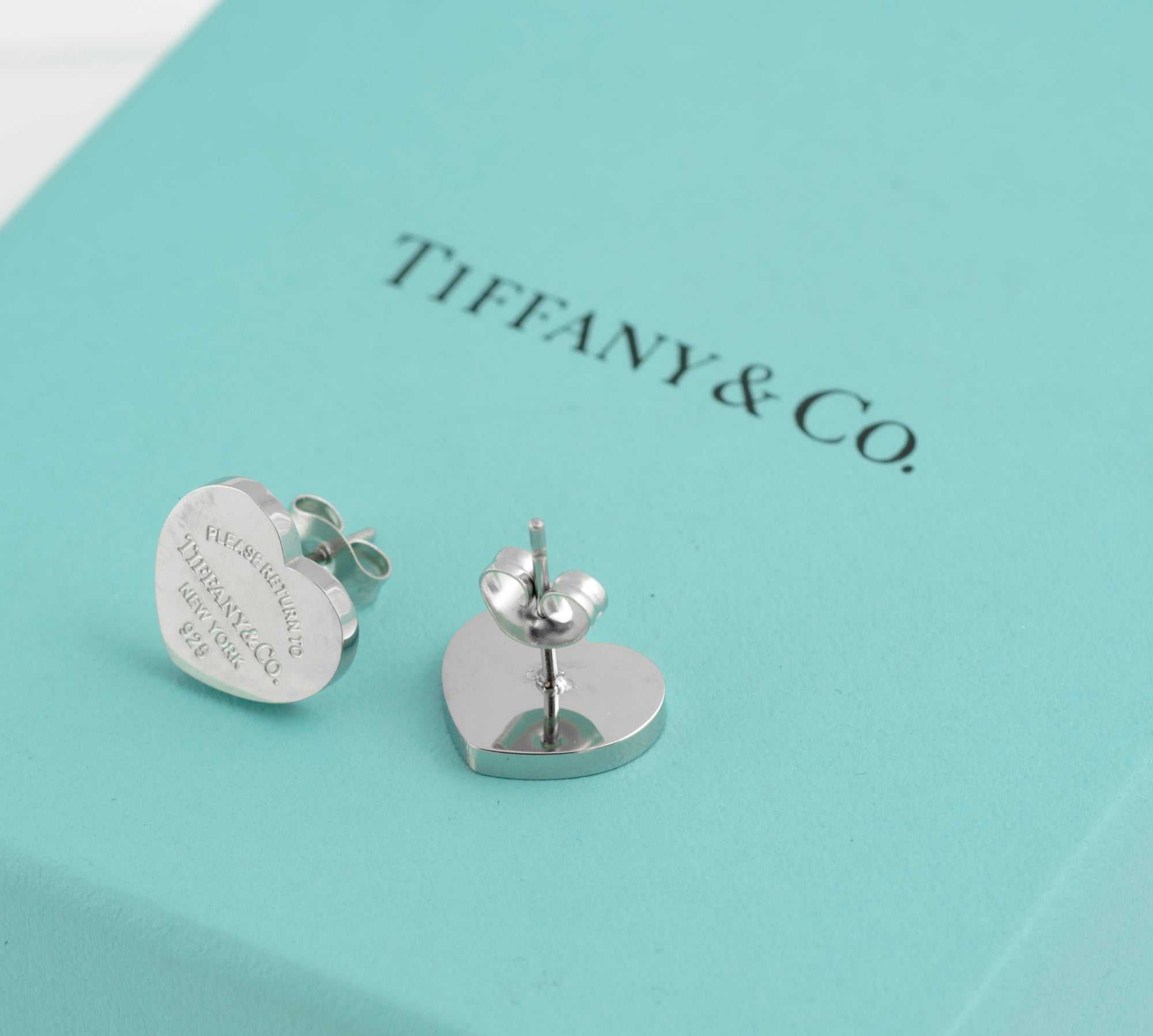 Pair of Tiffany and Co Return to Tiffany sterling silver heart stud earrings on Tiffany blue box showing plain polished reverse of one earring and post and butterfly back fitting of second earring