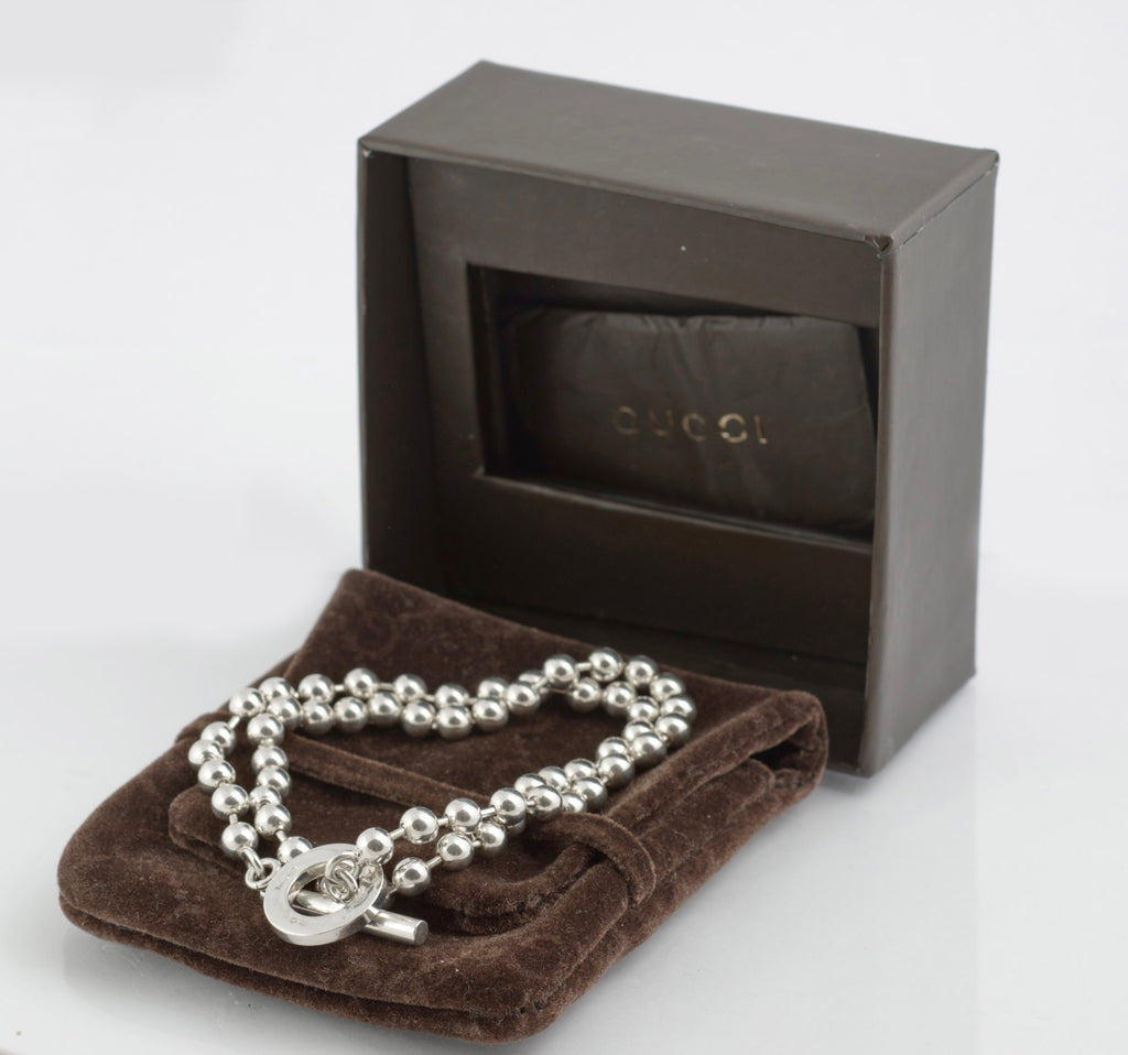 Vintage Gucci Boule sterling silver ball link necklace laid on dark brown Gucci soft logo pouch on white background showing full length of ball link chain and toggle clasp