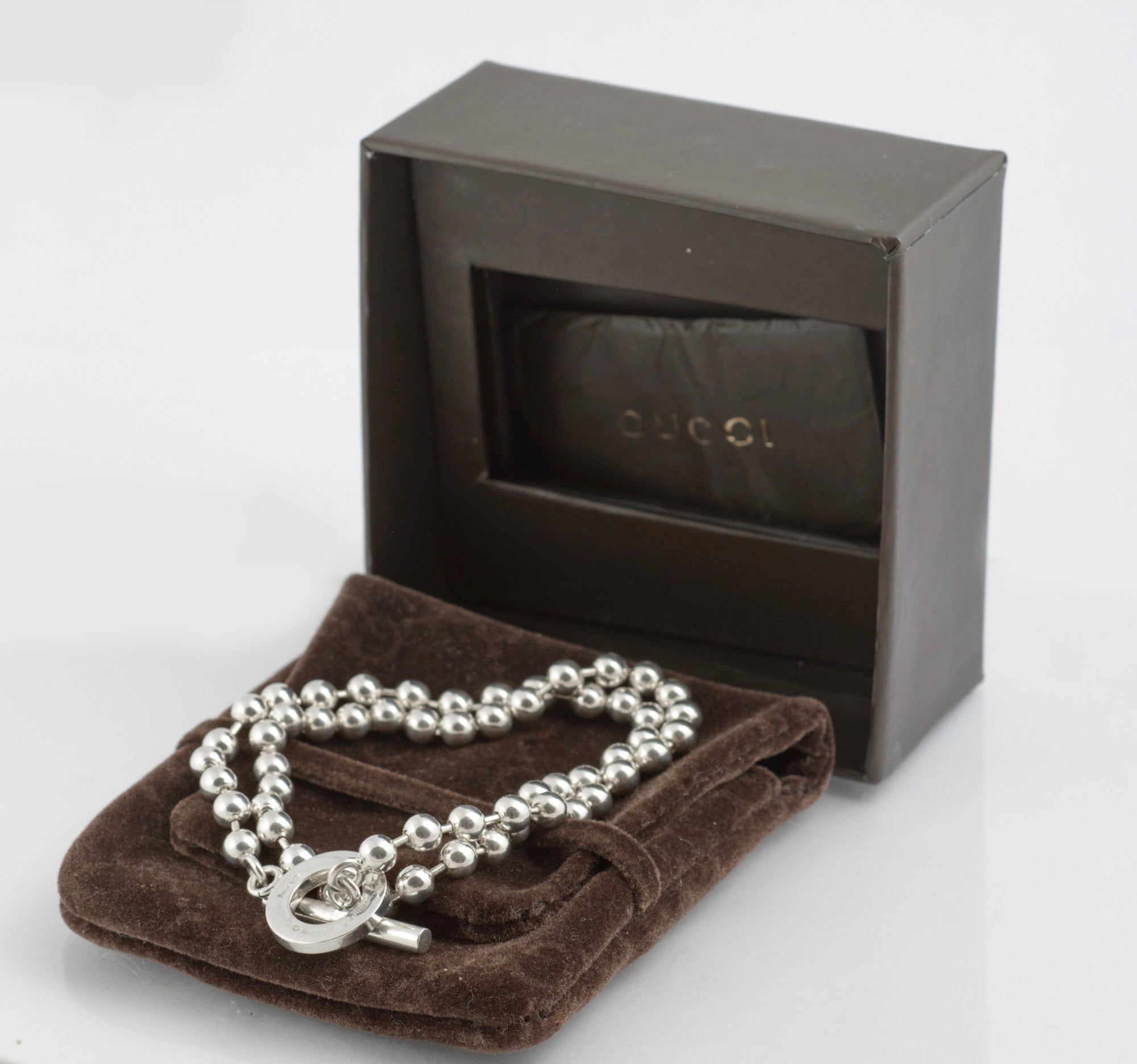 Vintage Gucci Boule sterling silver ball link necklace laid on dark brown Gucci soft logo pouch on white background showing full length of ball link chain and toggle clasp