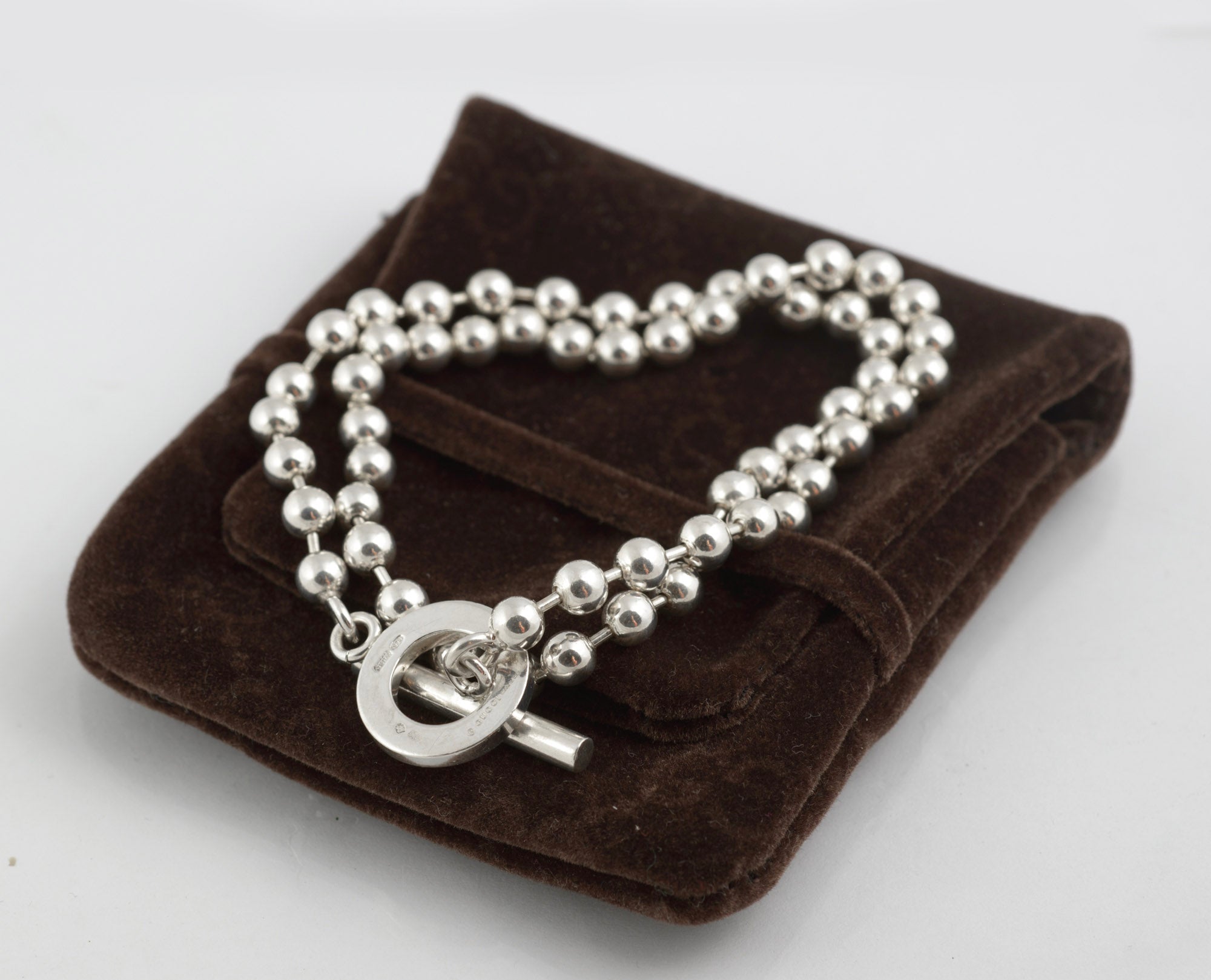 Close up of Gucci Boule sterling silver toggle ring showing Gucci engraved to upper face of ring and ball link chain connections on dark brown velvet background