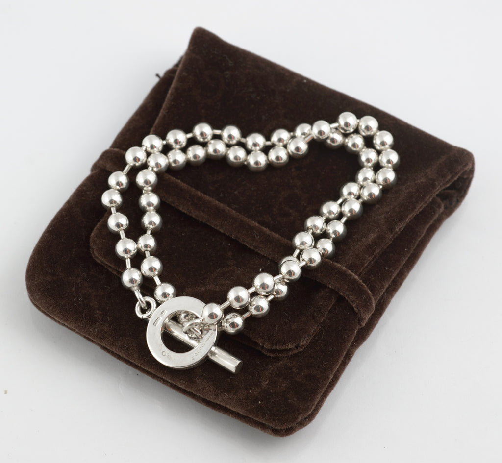 Close up of Gucci Boule sterling silver toggle clasp mechanism showing circular ring and T bar pendant hanging from ball link chain on white background
