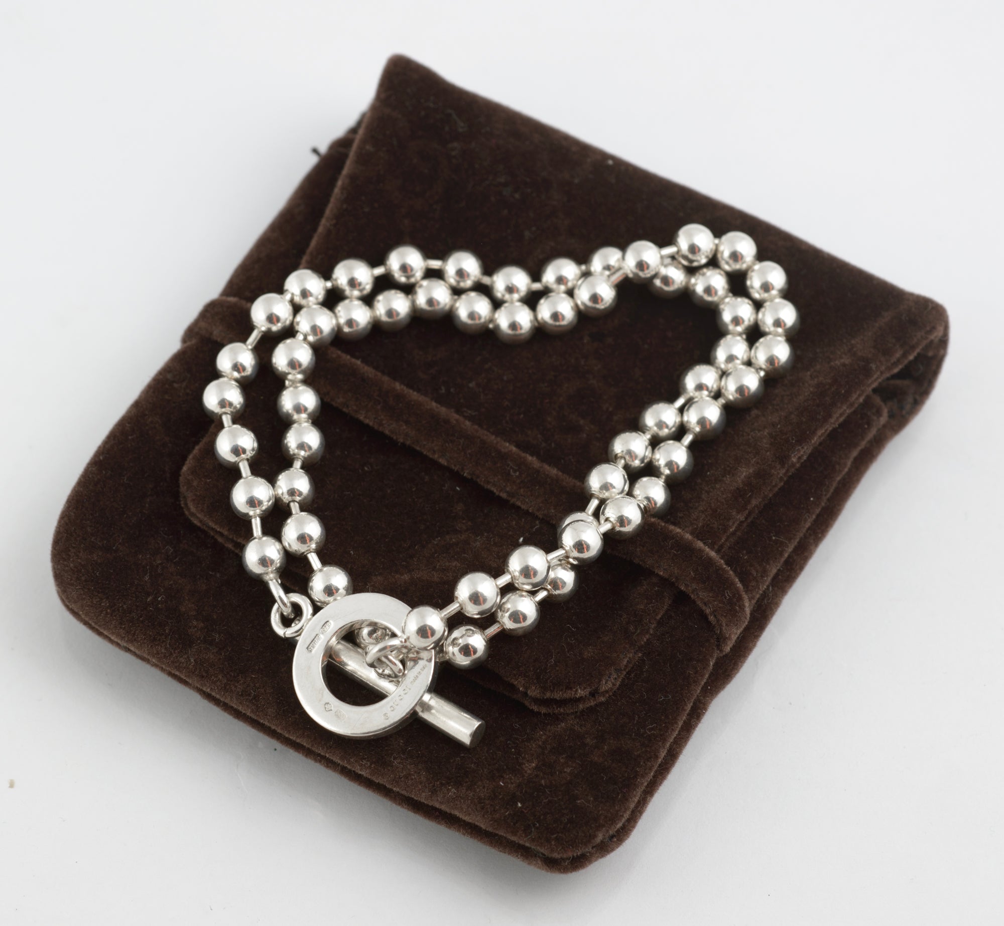 Close up of Gucci Boule sterling silver toggle clasp mechanism showing circular ring and T bar pendant hanging from ball link chain on white background