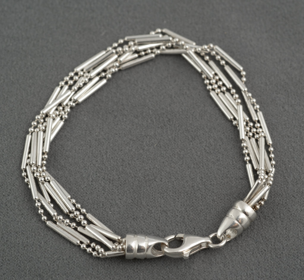 Vintage sterling silver six strand bar and bead bracelet with tapered torpedo terminals and lobster clasp laid in circle on dark grey background showing full construction