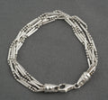 Vintage sterling silver six strand bar and bead bracelet with tapered torpedo terminals and lobster clasp laid in circle on dark grey background showing full construction