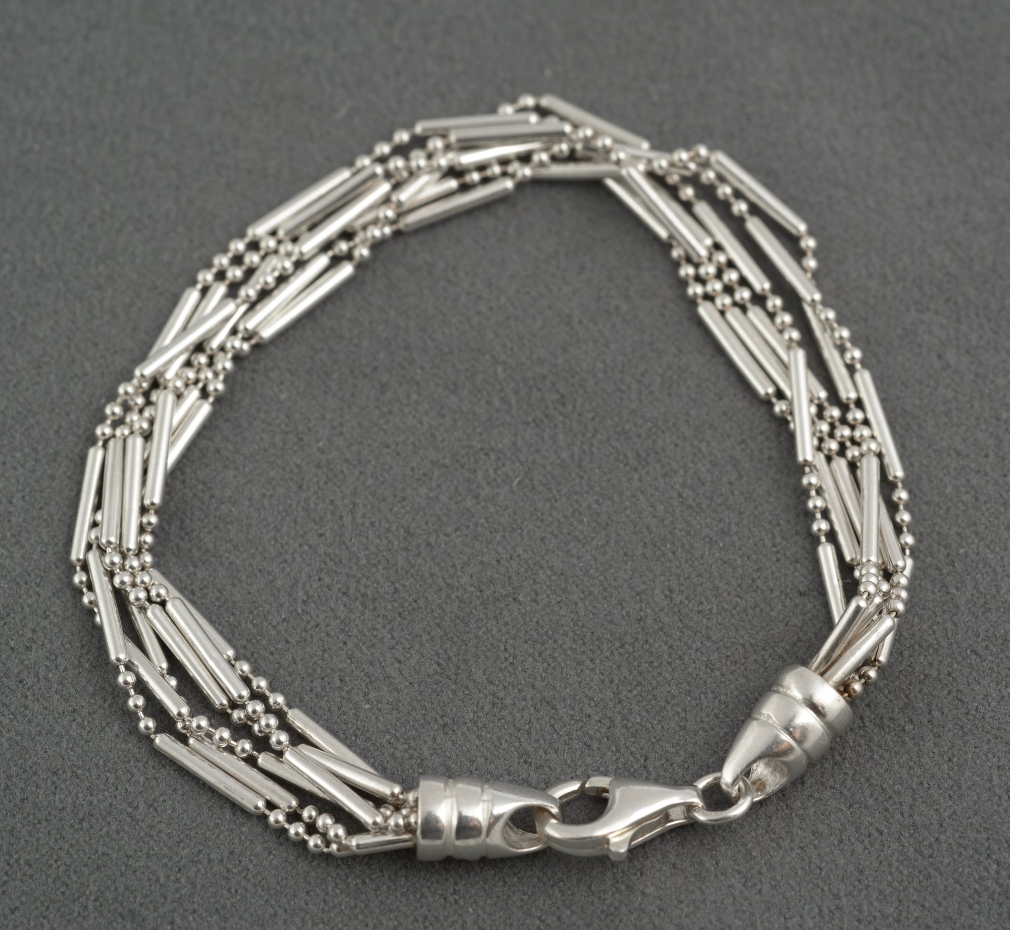 Vintage sterling silver six strand bar and bead bracelet with tapered torpedo terminals and lobster clasp laid in circle on dark grey background showing full construction
