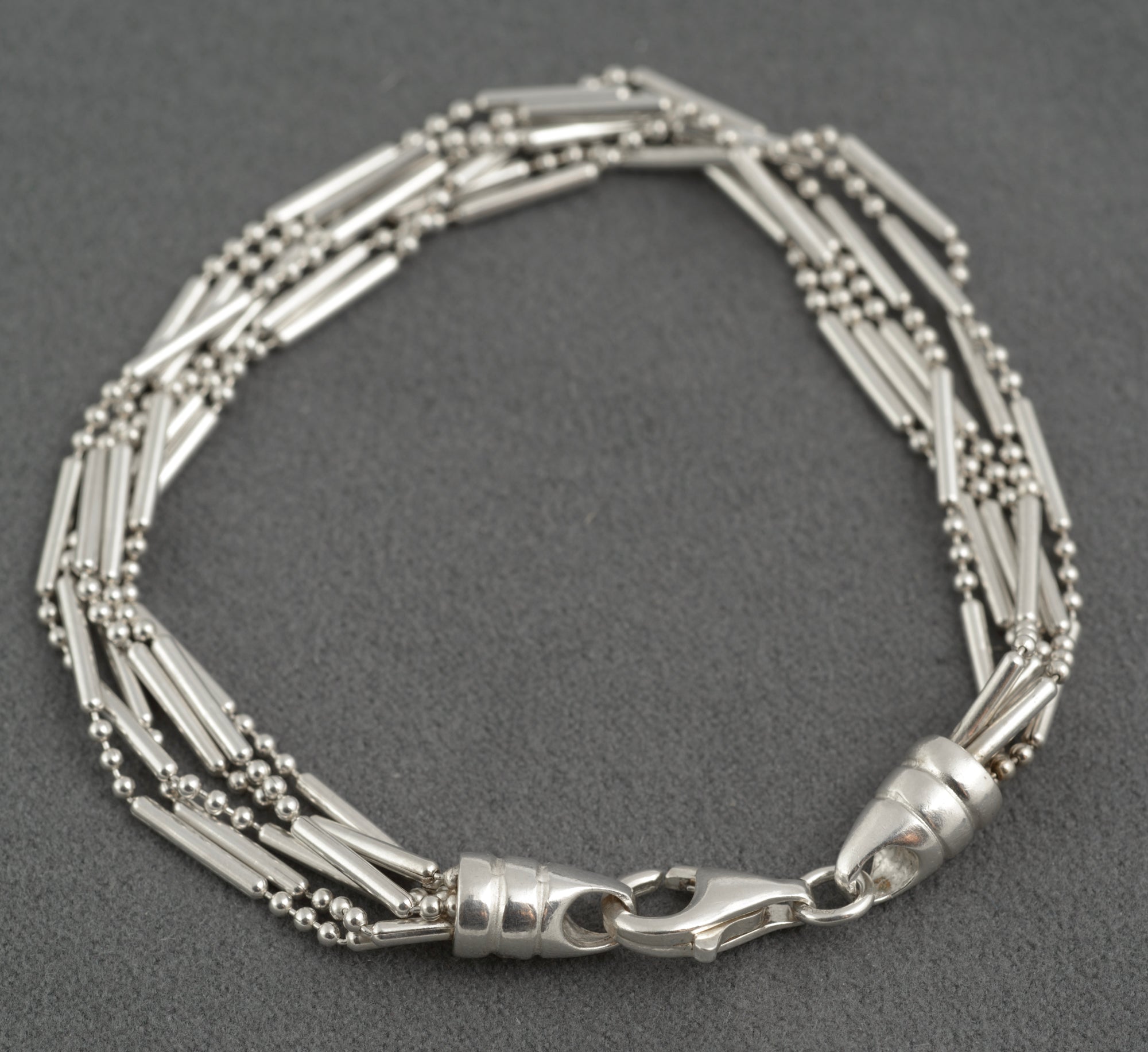 Vintage sterling silver six strand bar and bead bracelet close up of lobster clasp and tapered torpedo terminal gathering all six strands on dark grey background