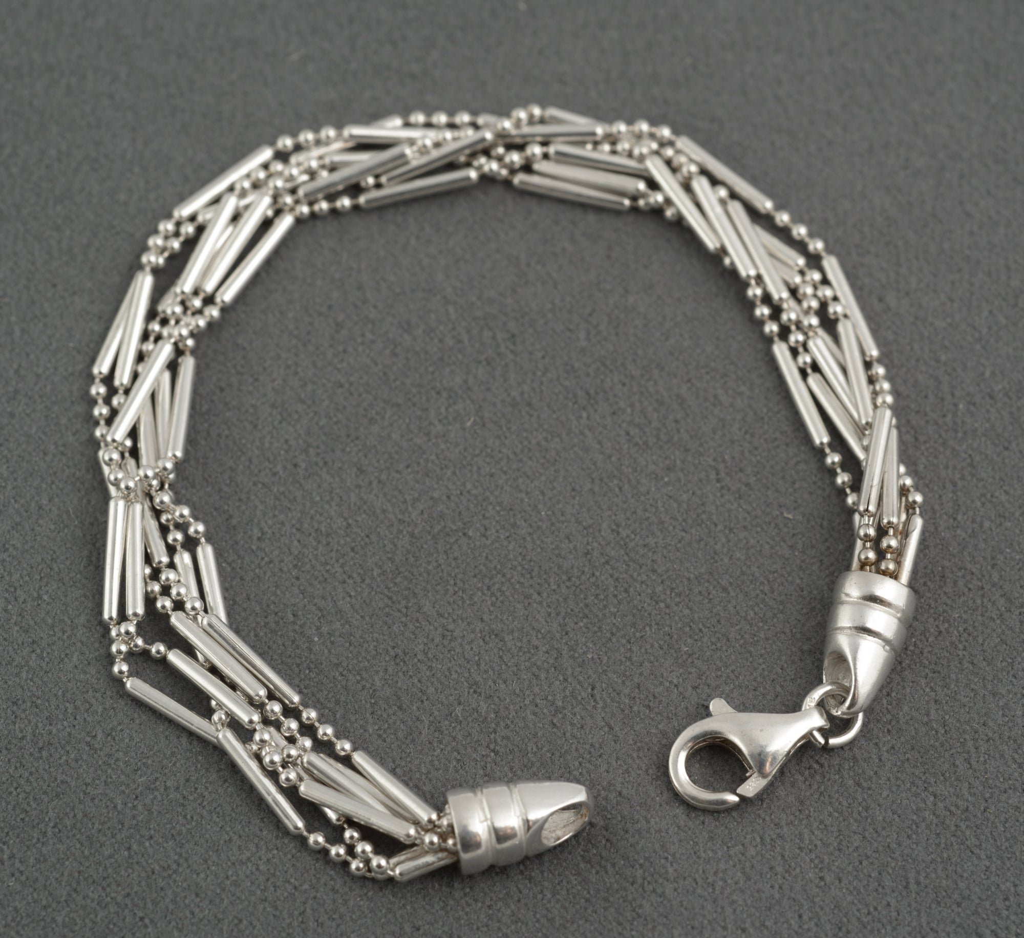 Vintage sterling silver six strand bar and bead bracelet open clasp view showing both tapered torpedo terminals and lobster clasp with connecting ring on dark grey background