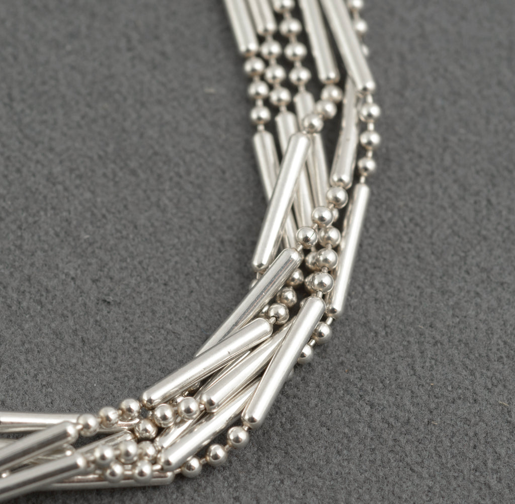 Close up detail of vintage sterling silver six strand bracelet showing three parallel polished bar links flanked by two bead chains gathered at nodal points on dark grey background