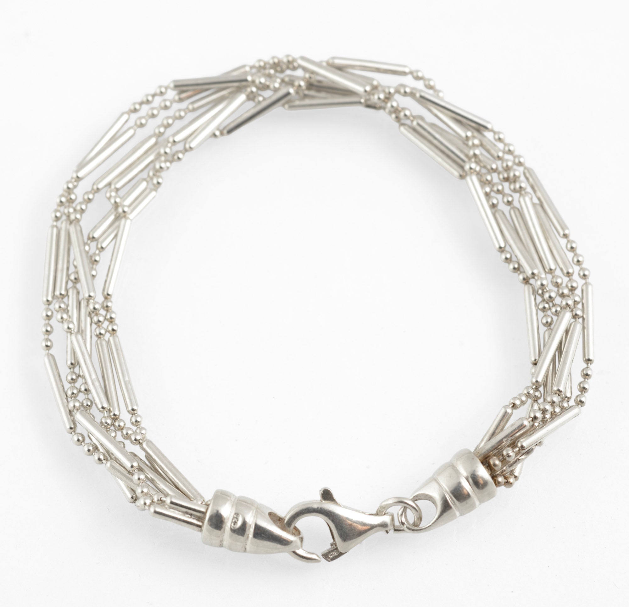Vintage sterling silver six strand bar and bead bracelet with tapered torpedo terminals and lobster clasp laid in circle on white background showing full length 19cm construction