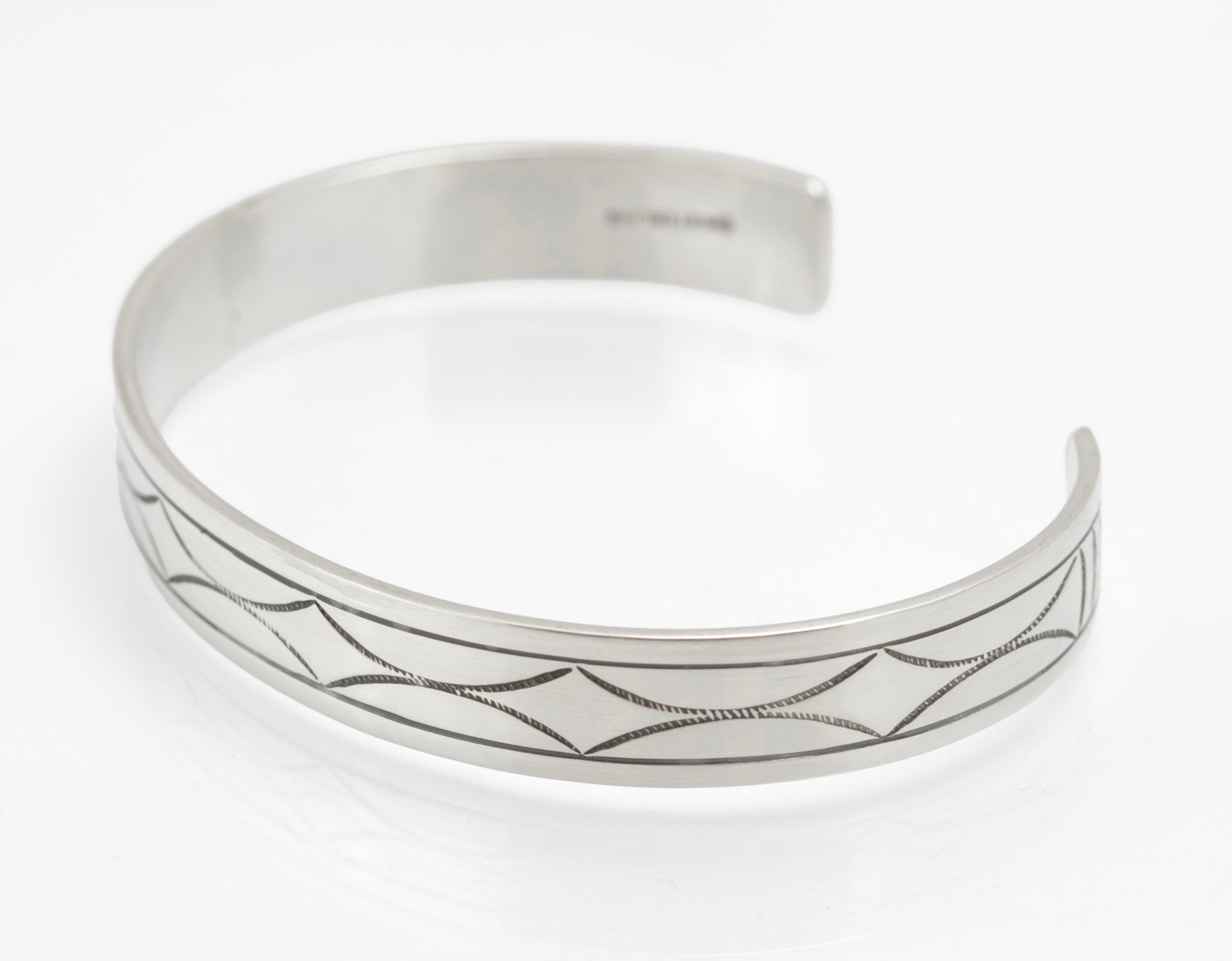 Inside of vintage sterling silver cuff bangle showing pictorial maker's mark and STERLING stamp on white background
