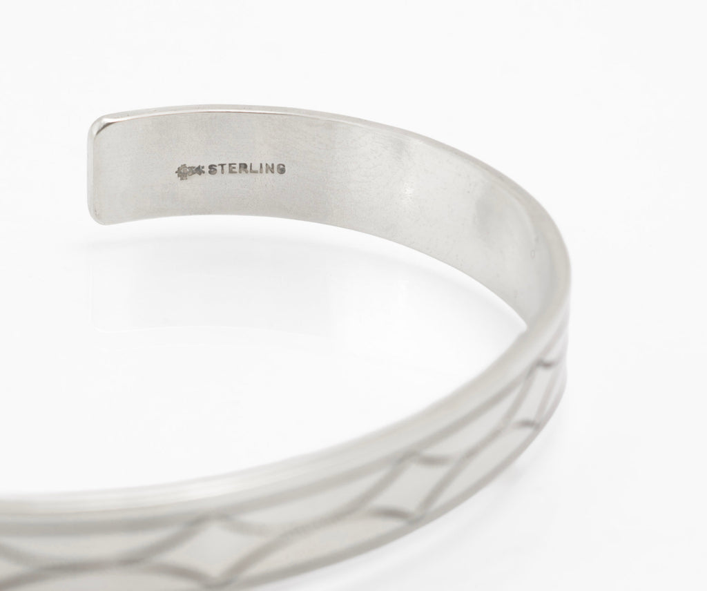 Vintage sterling silver open cuff bangle displayed on dark grey suede cone showing engraved geometric star pattern and scale on white background