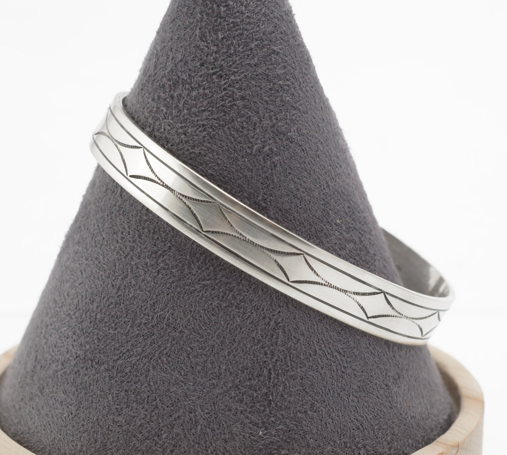 Vintage sterling silver open cuff bangle low angle view showing hand engraved geometric decoration and tapered band profile on white background