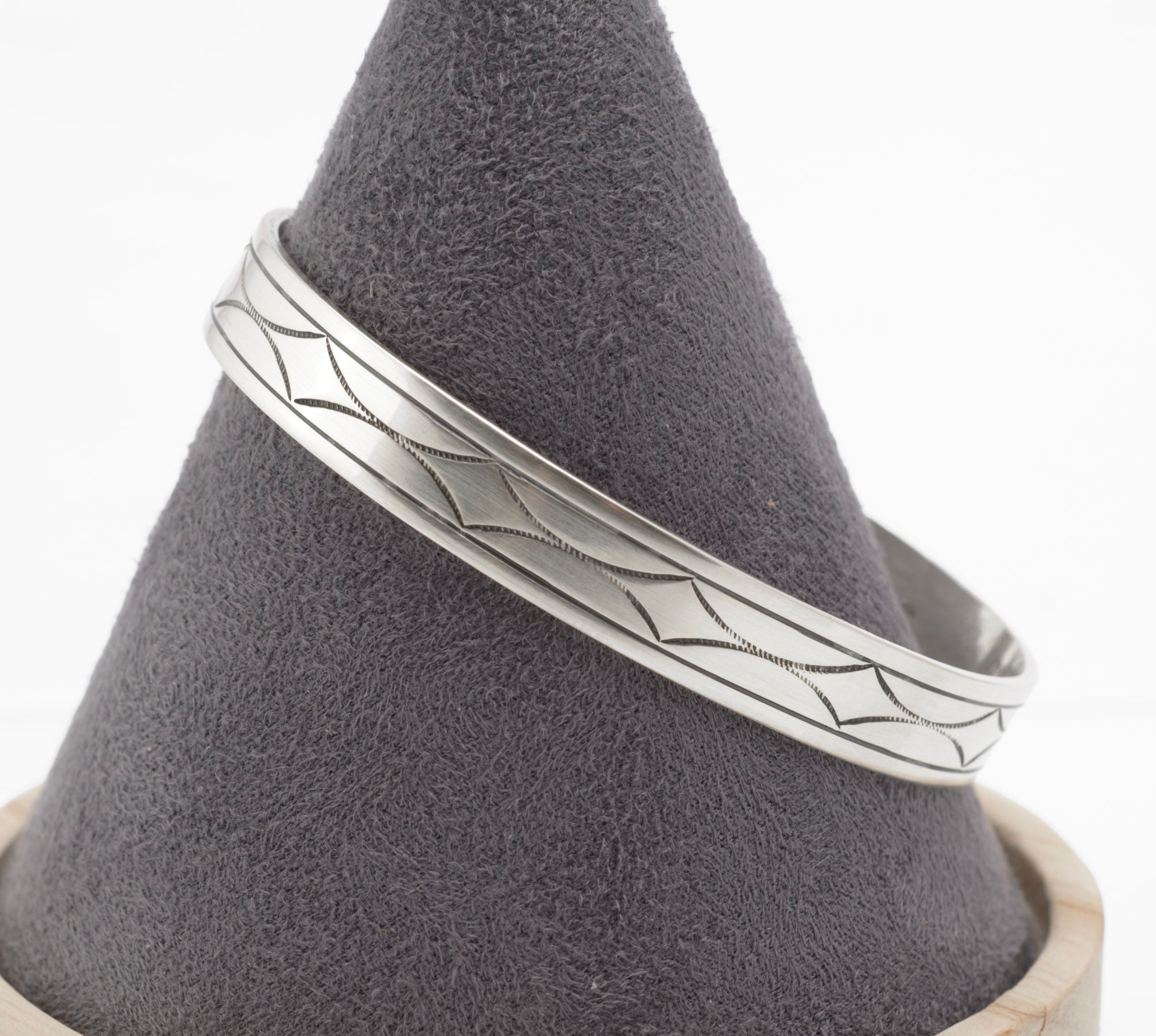 Vintage sterling silver open cuff bangle low angle view showing hand engraved geometric decoration and tapered band profile on white background