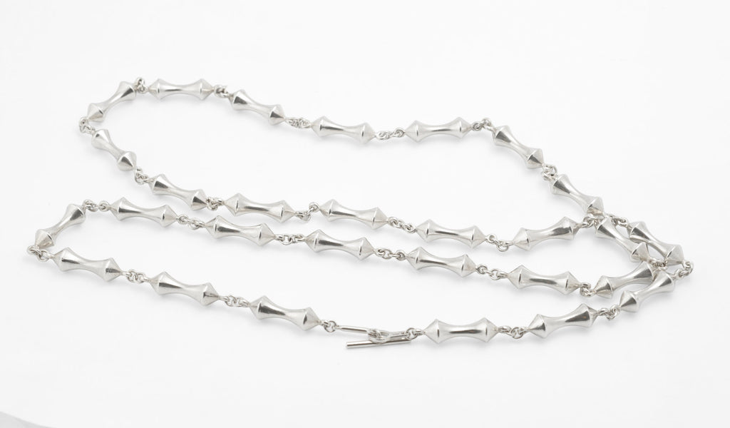 Vintage sterling silver long necklace with sculptural double cone reel links joined by fine chain laid flat on white background showing full 93cm length and T-bar toggle clasp