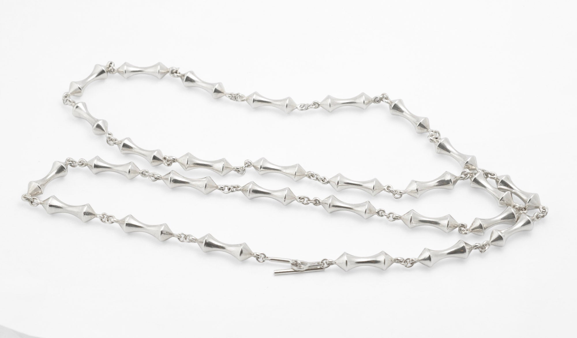 Vintage sterling silver long necklace with sculptural double cone reel links joined by fine chain laid flat on white background showing full 93cm length and T-bar toggle clasp