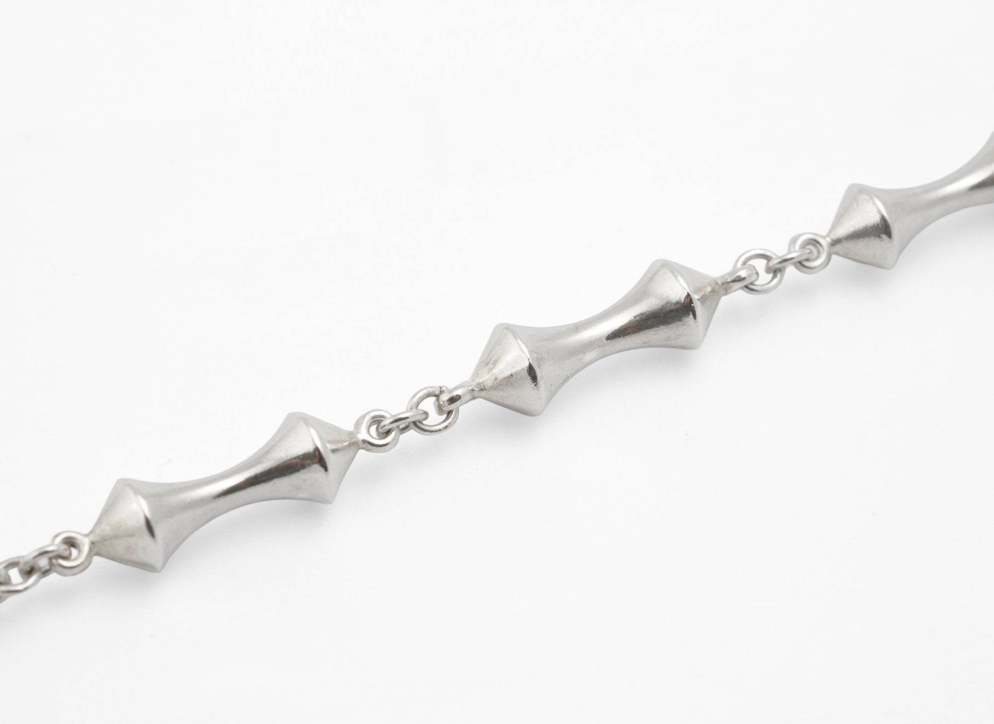 Close up of vintage sterling silver necklace double cone reel links showing narrow waist and faceted polished surfaces with fine connecting chain on white background