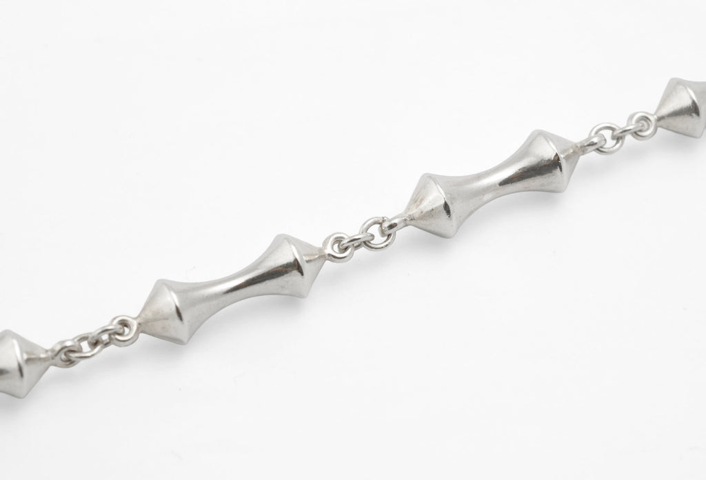 Detail of vintage sterling silver necklace showing double cone reel links with opposing pointed cone ends meeting at narrow waist joined by round link chain on white background