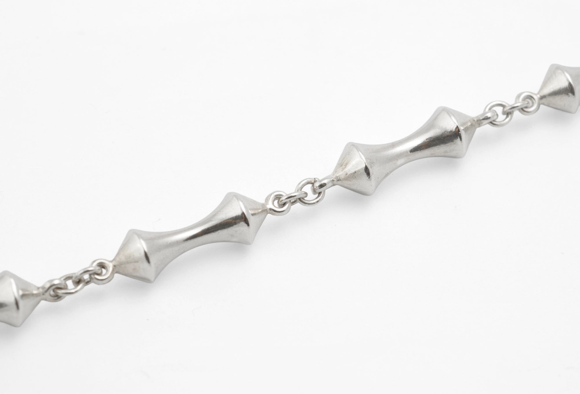 Detail of vintage sterling silver necklace showing double cone reel links with opposing pointed cone ends meeting at narrow waist joined by round link chain on white background